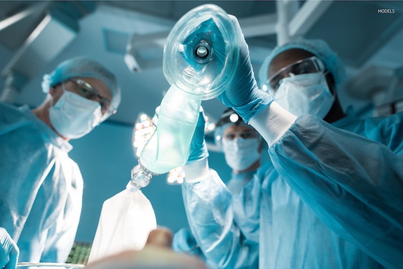 Surgical team surrounding patient and preparing anesthesia mask