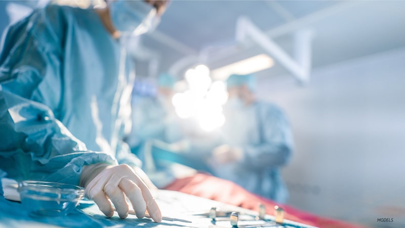 Surgeon reaching for tools in operating room.