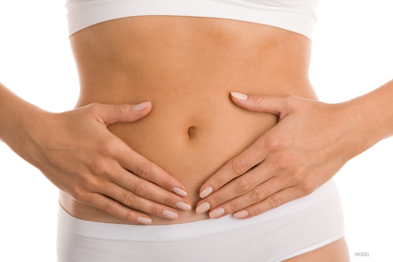 Woman with her hands surrounding belly button on abdomen.